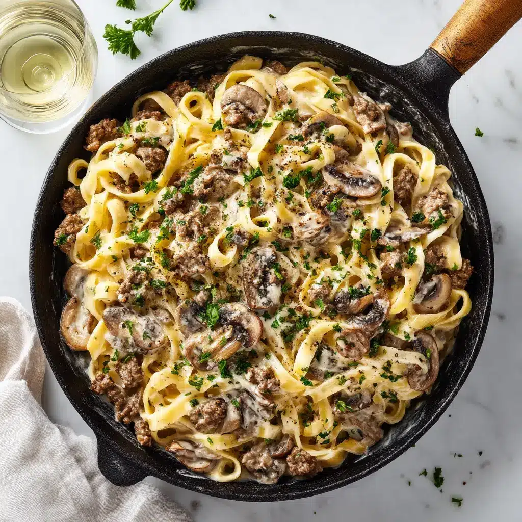 Rustic black cast-iron skillet filled with Ground Beef Pasta Alfredo, savory mushrooms, and thick parmesan cream sauce.