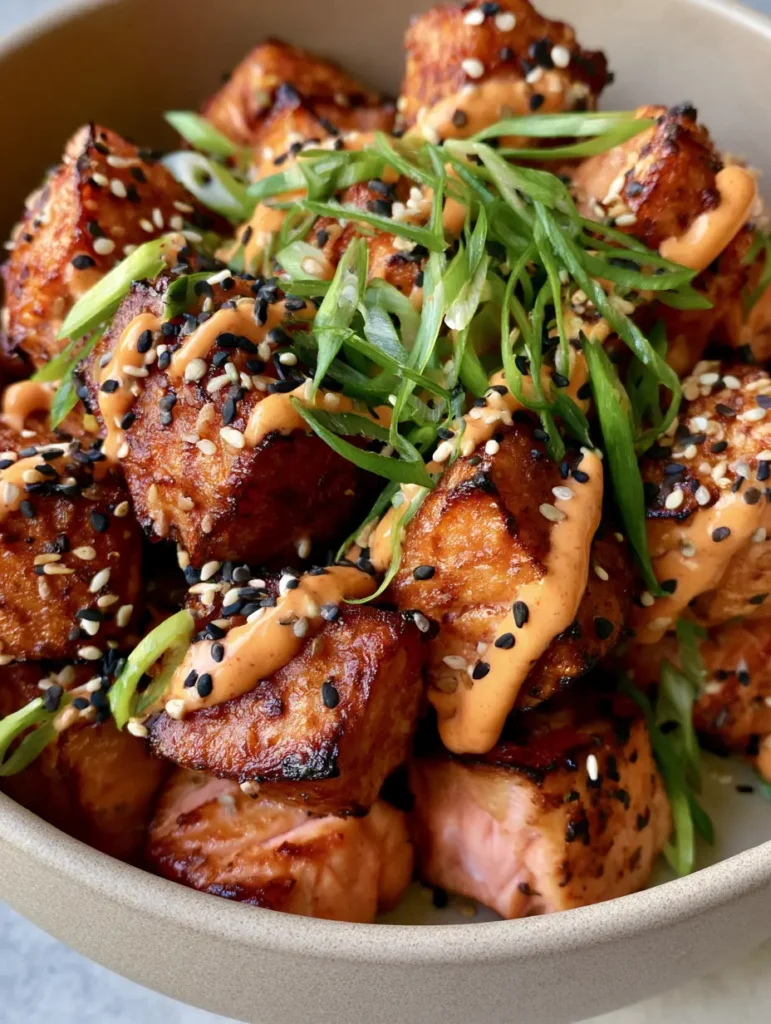 A pile of Crispy Bang Bang Salmon Bites in a neutral matte ceramic bowl illuminated by soft natural light.