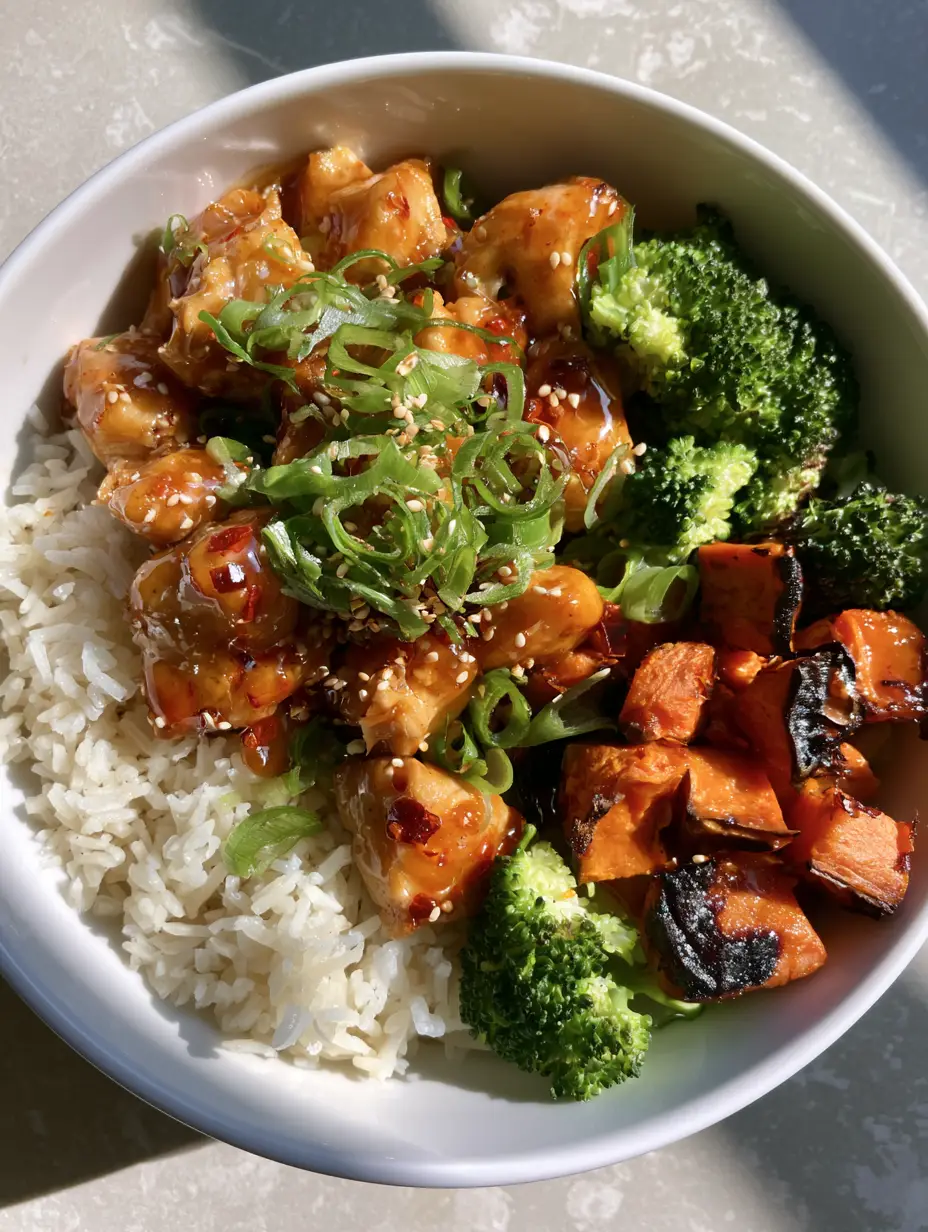 A high-angle view of a professional white bowl layout of Hot Honey Chicken Bowls over long-grain white rice with caramelized sweet potato cubes.