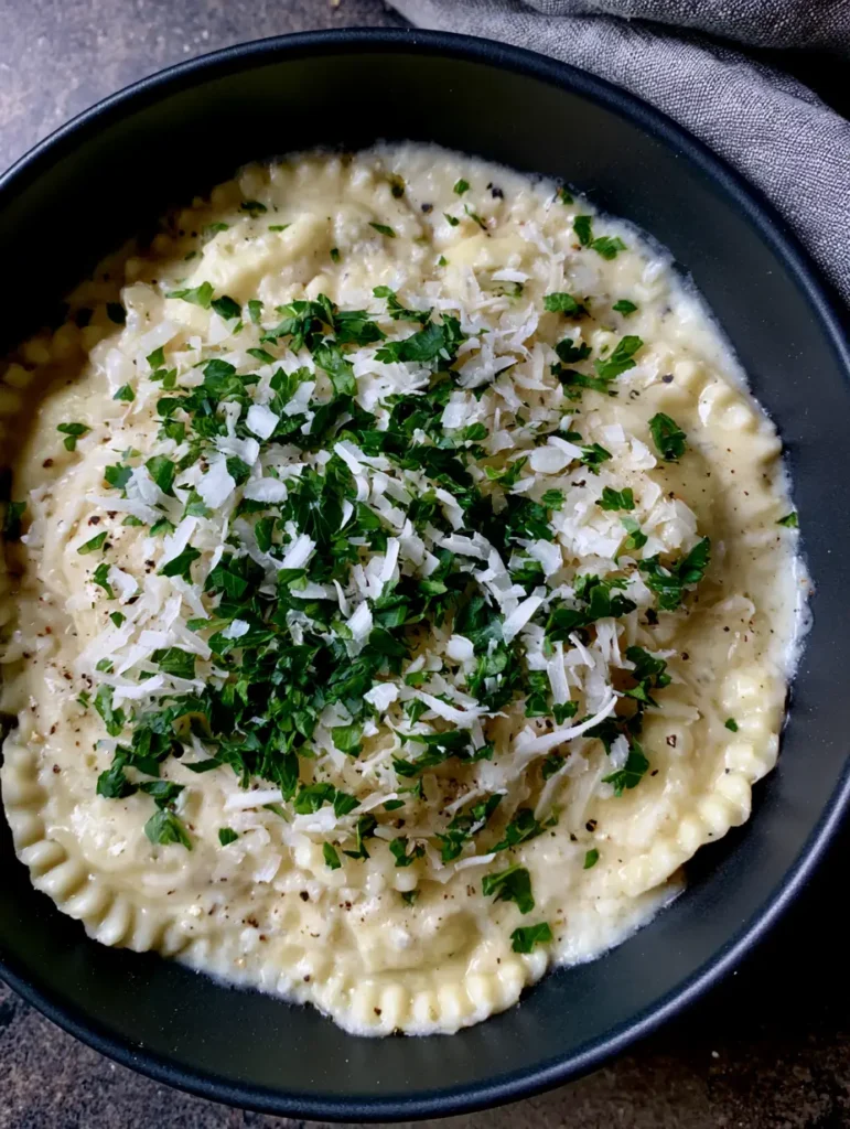 Creamy Garlic Parmesan Ravioli with Fresh Parsley 1 Overhead smartphone photo of Creamy Garlic Parmesan Ravioli with parsley and black pepper flakes on a rustic surface.